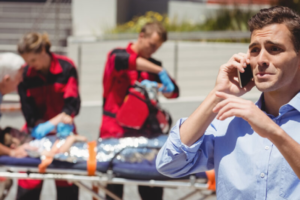 Distraught man makes a cellphone call while EMTs attend to injured child on a stretcher.