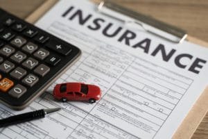 Image of calculator and insurance paperwork with a tiny red toy car.