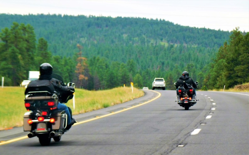 Two touring motorcycles driving down the highway with a wooded hill in the background.